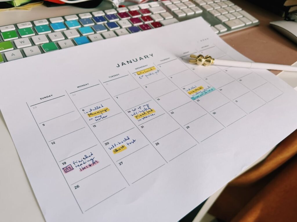 a photo showing a printout of a calendar for January 2025 with empty boxes for each day and a handful of descriptions about actions I have taken (like install Phanpy) in a color-coded way